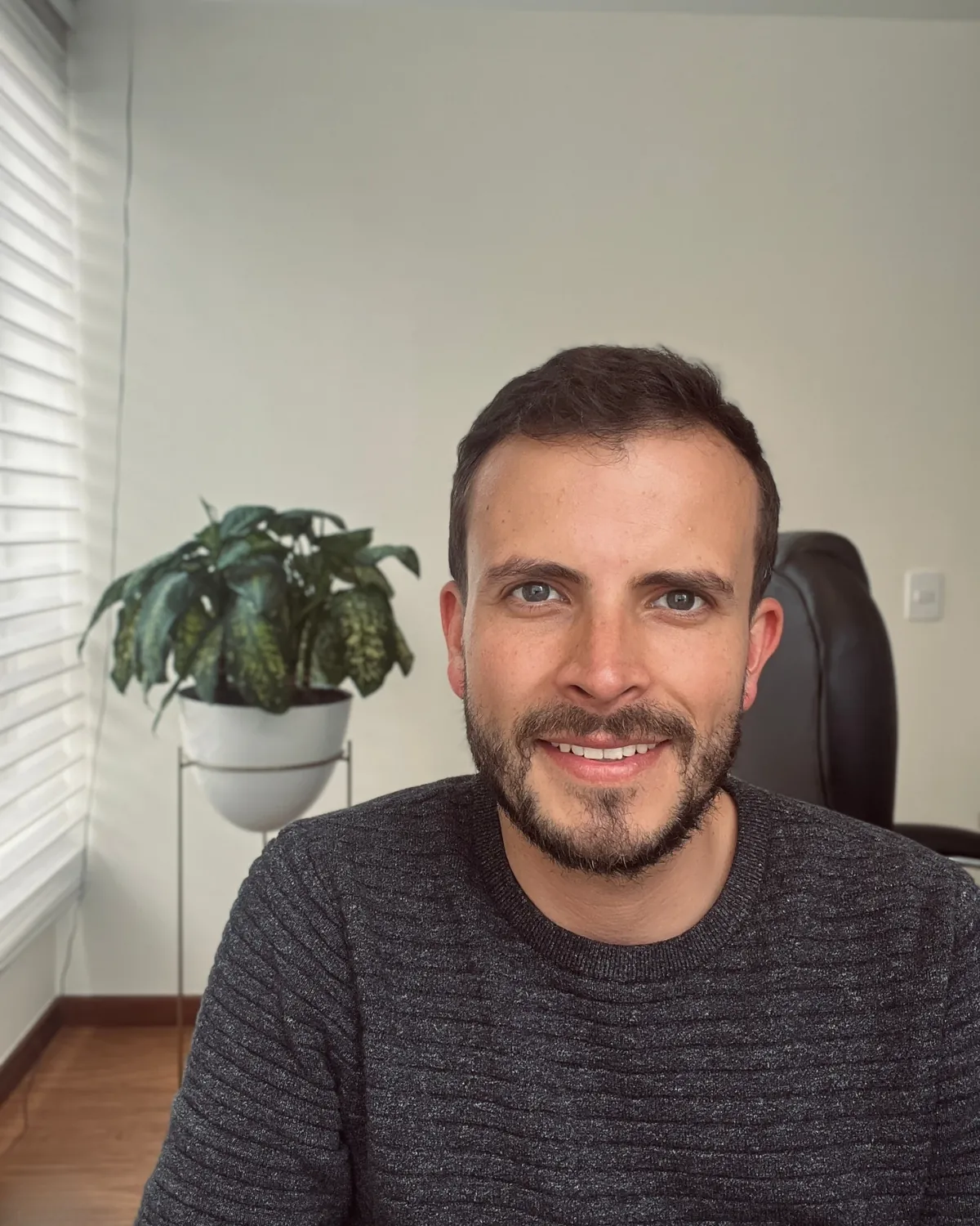Sergio Franco sonriendo, con barba y suéter gris oscuro, en su oficina