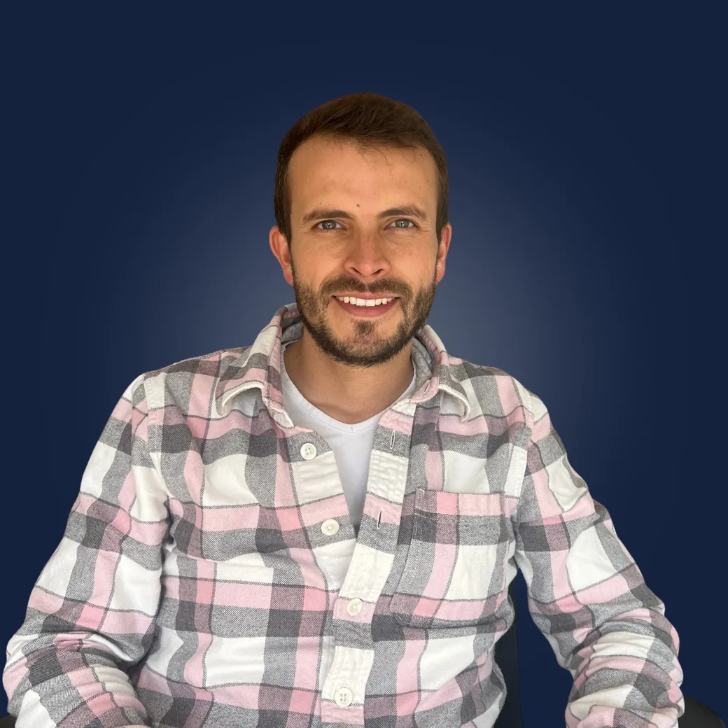 Sergio Franco sonriendo, con camisa a cuadros, sobre fondo azul oscuro